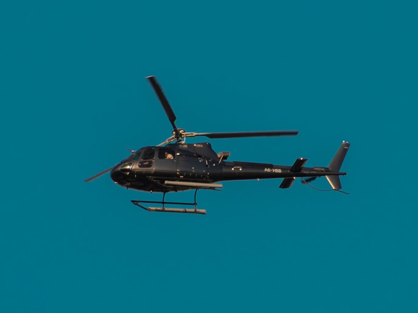 A black helicopter in flight against clear sky, carrying a UAE A6 registration