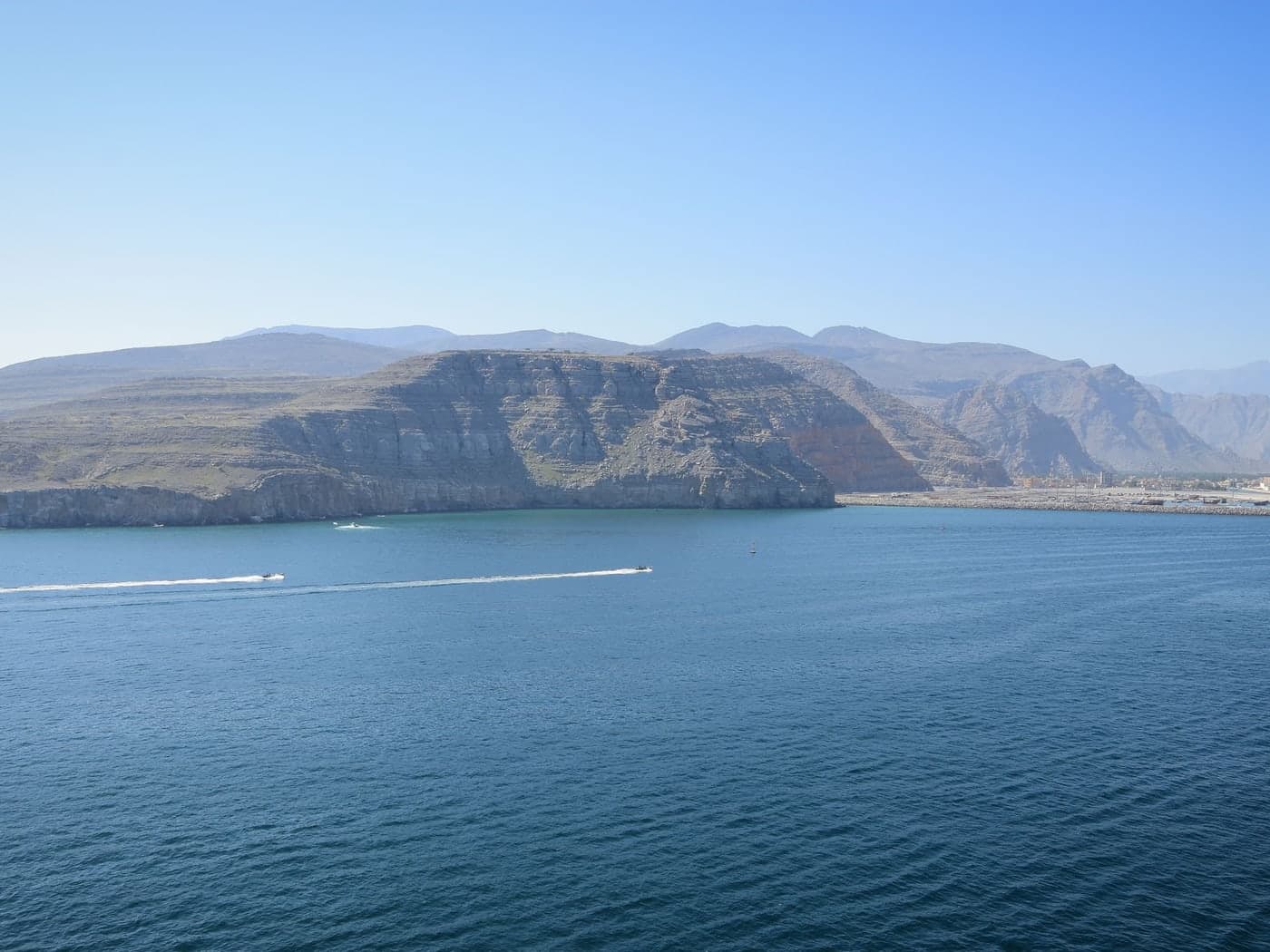 The rugged limestone coastline of the Musandam peninsula meeting deep blue water, with Khasab on the shore beyond
