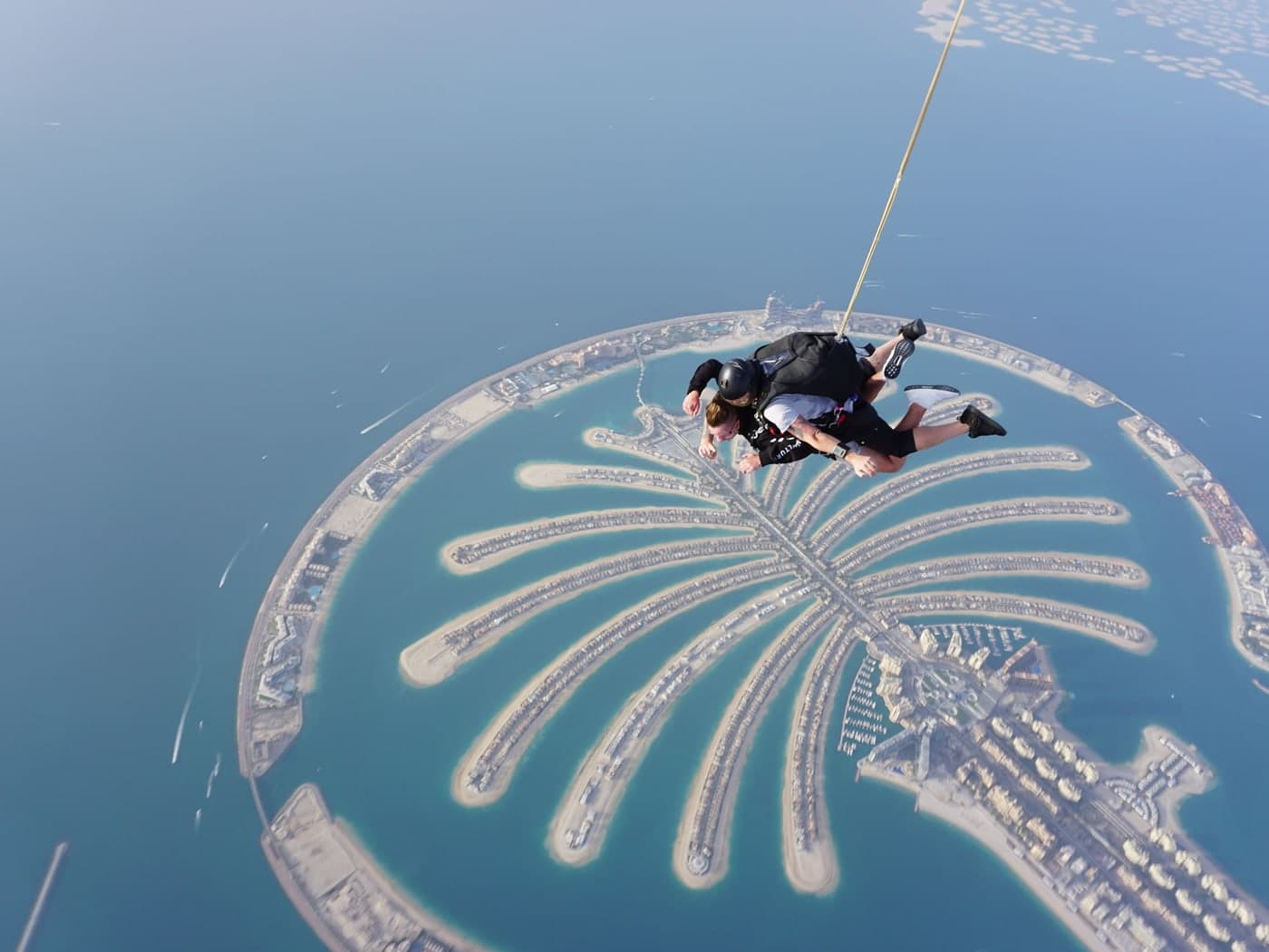 A tandem skydive in freefall high above Palm Jumeirah, the whole island and its fronds laid out in the sea below