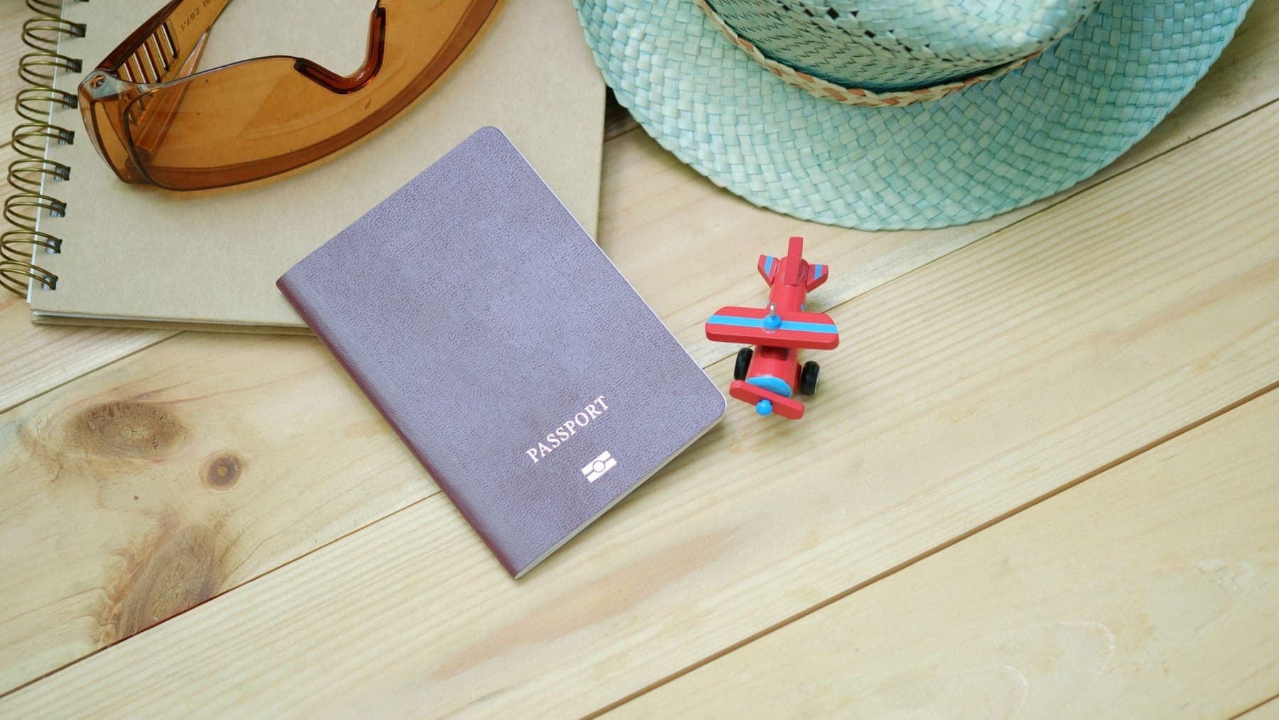A plain grey passport marked only with the word PASSPORT and the biometric chip symbol, on pale pine beside a kraft notebook