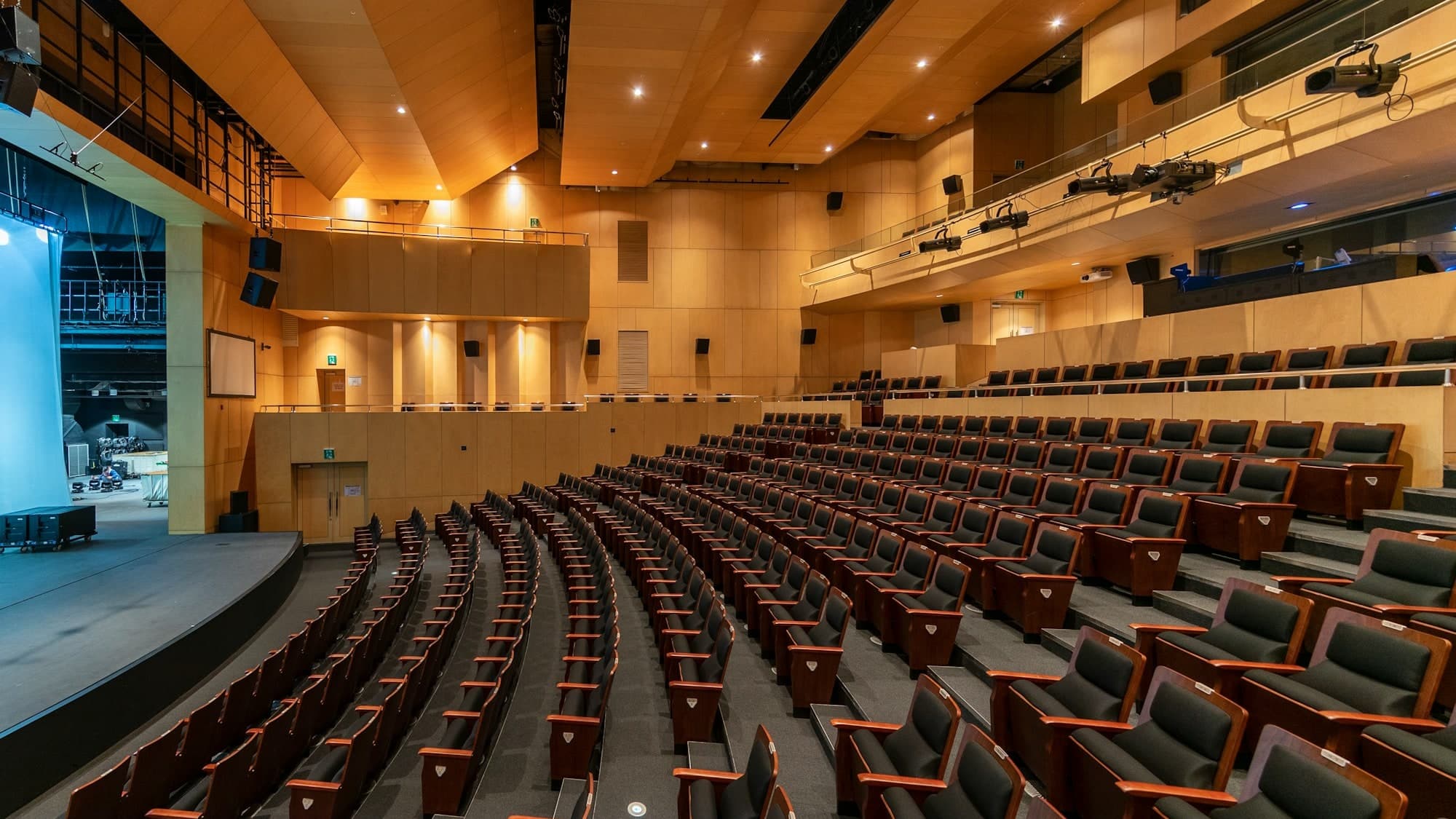 An empty auditorium seen from the stage, curved rows of seating rising under warm timber walls