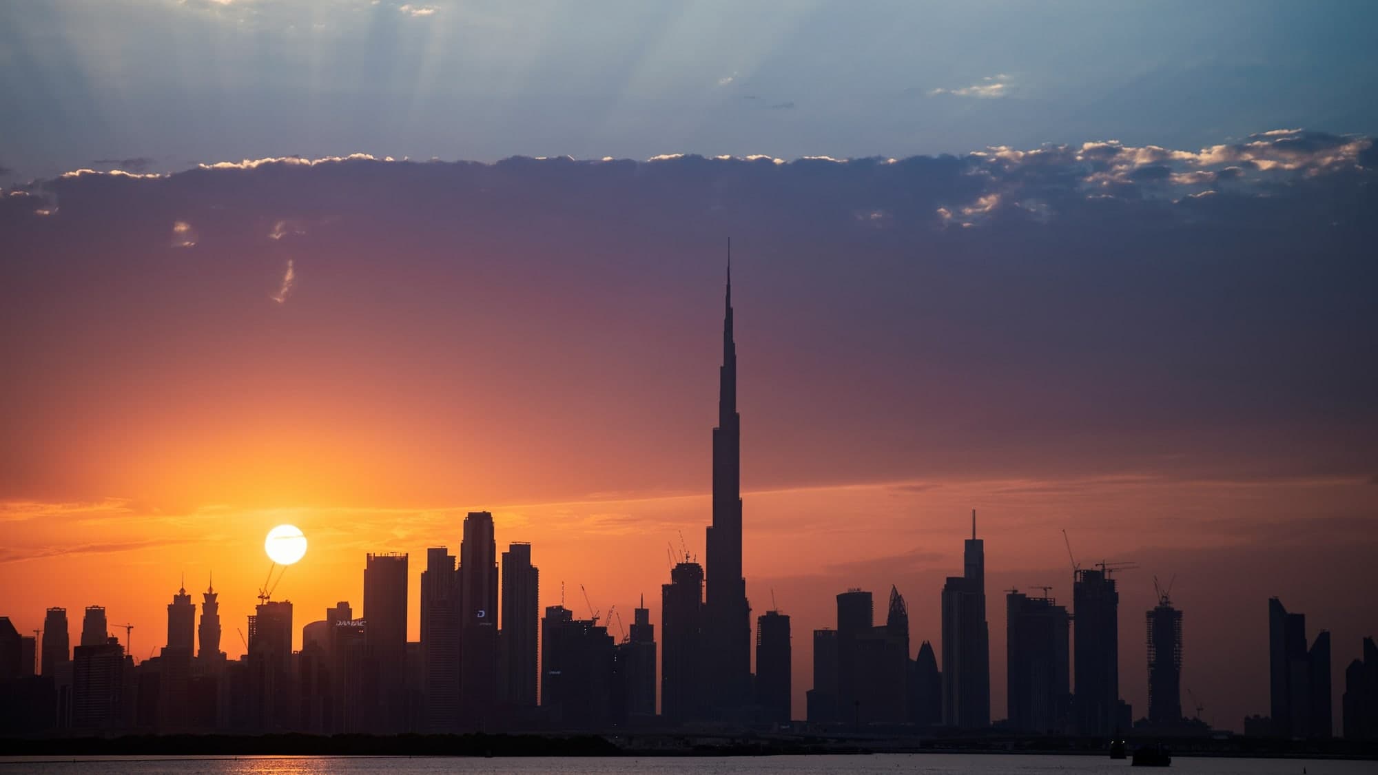 The Dubai skyline in silhouette at sunset, the sun sitting low beside the tallest towers