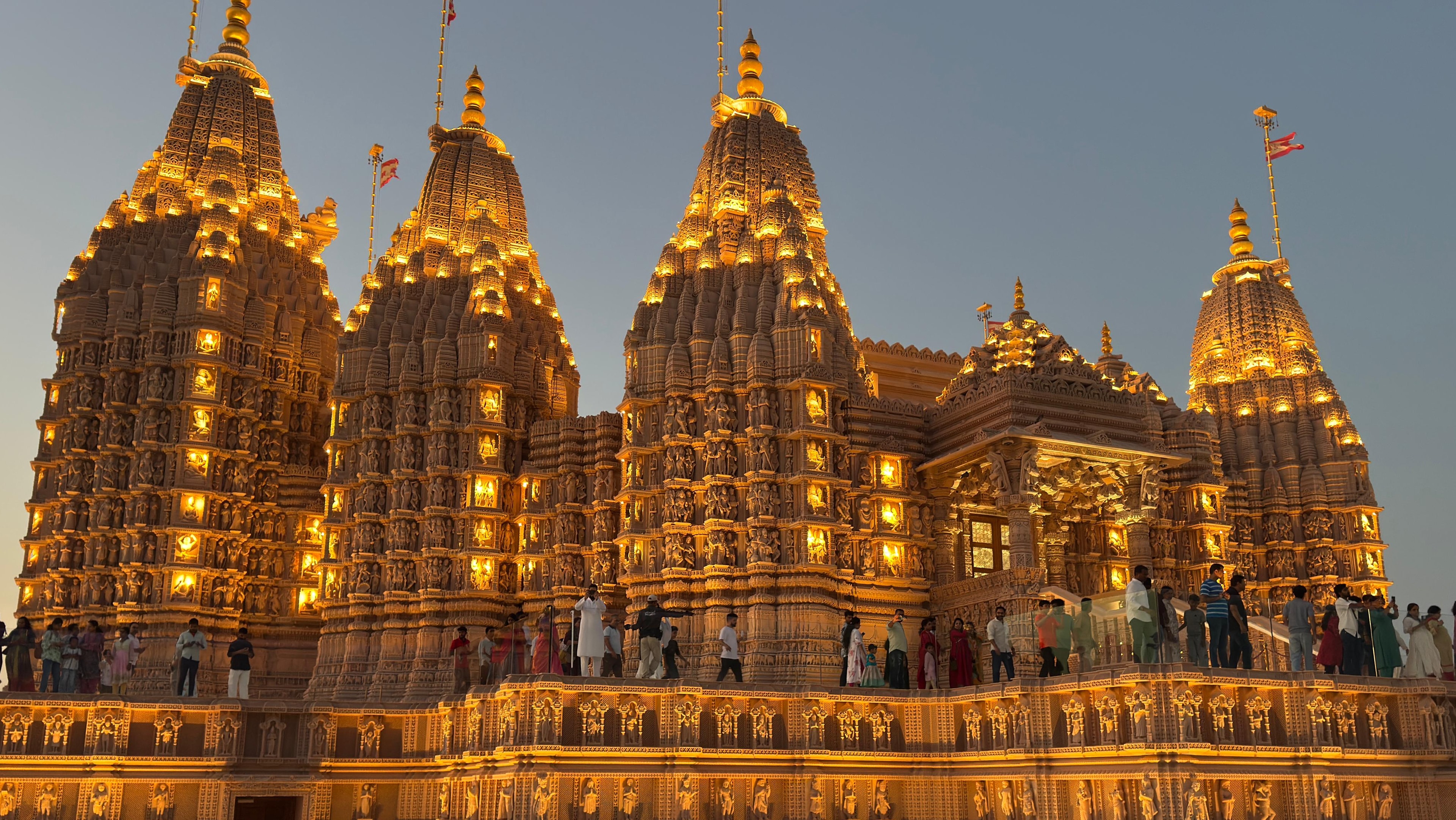 BAPS Hindu Mandir at Abu Mureikhah, Abu Dhabi, lit at dusk — its seven hand-carved sandstone spires above the plinth