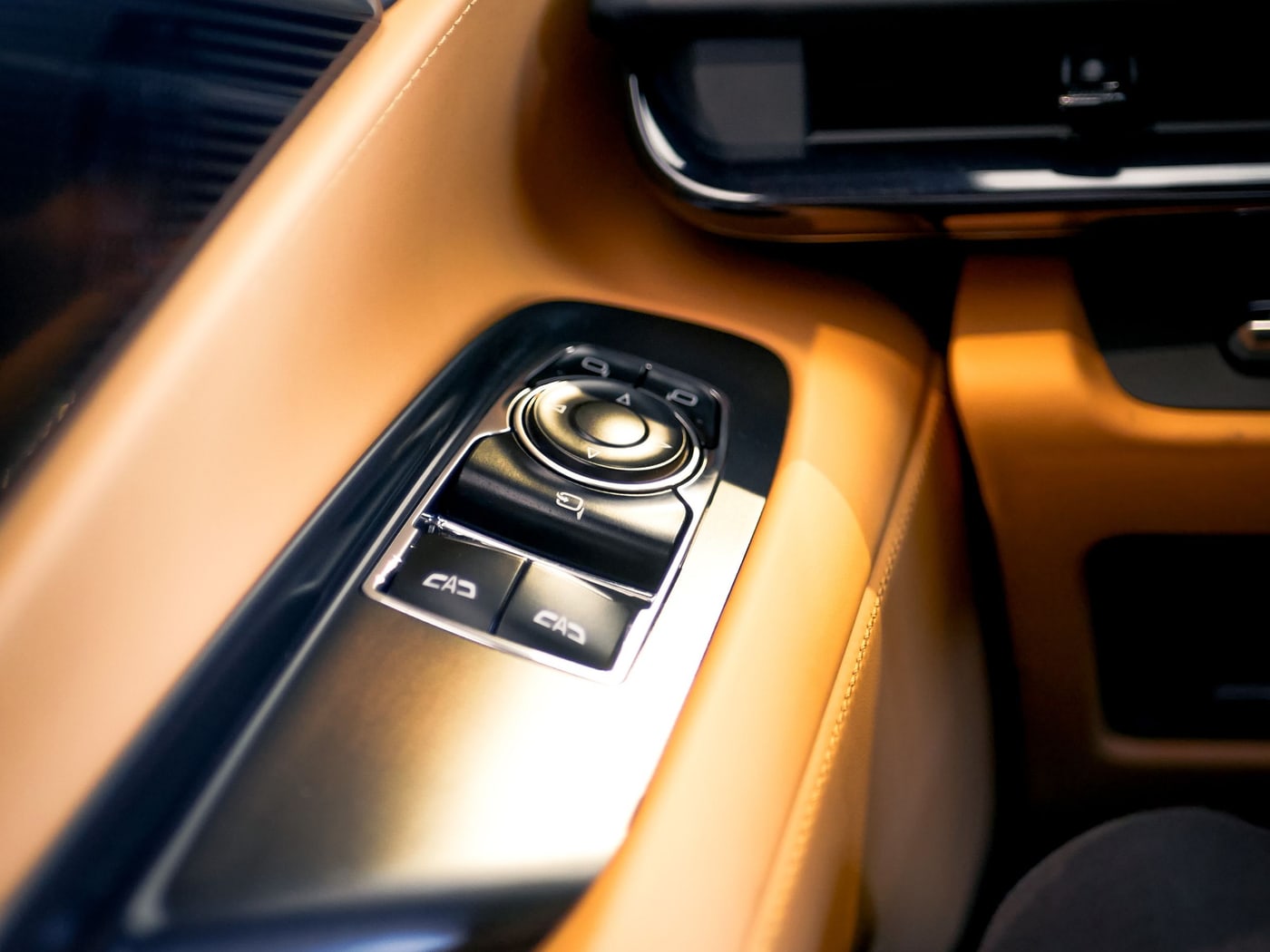 A close-up of an illuminated gear selector and centre console in a car interior, lit amber