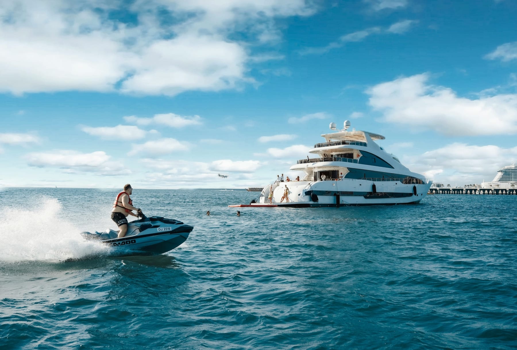 A private motor yacht on bright blue water with a jet ski crossing the foreground