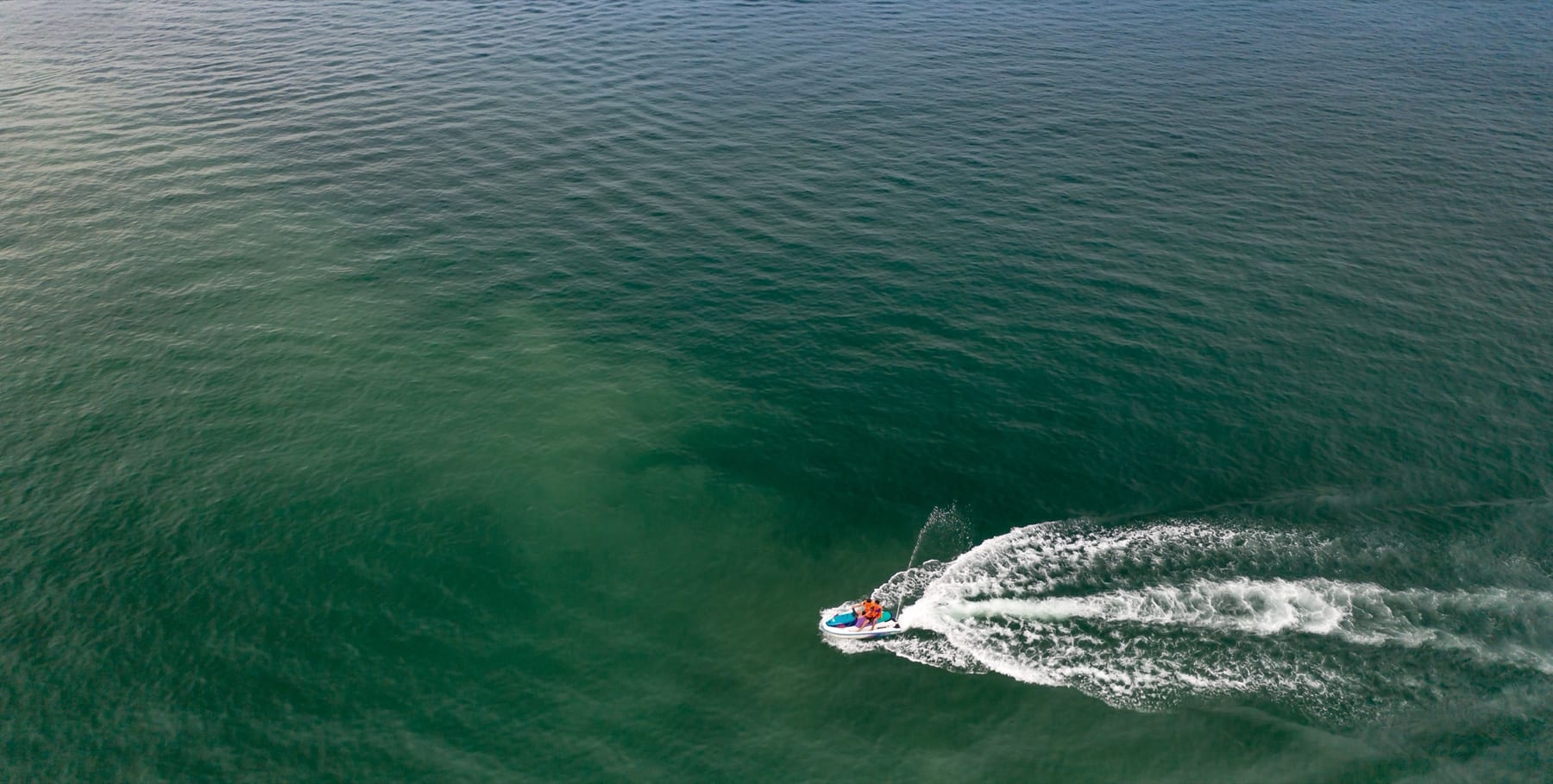 A rider carving across open blue water on a jet ski, leaving a bright white wake behind