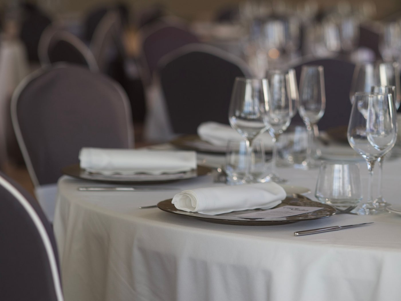 A banquet table laid with white linen, folded napkins and ranked wine glasses