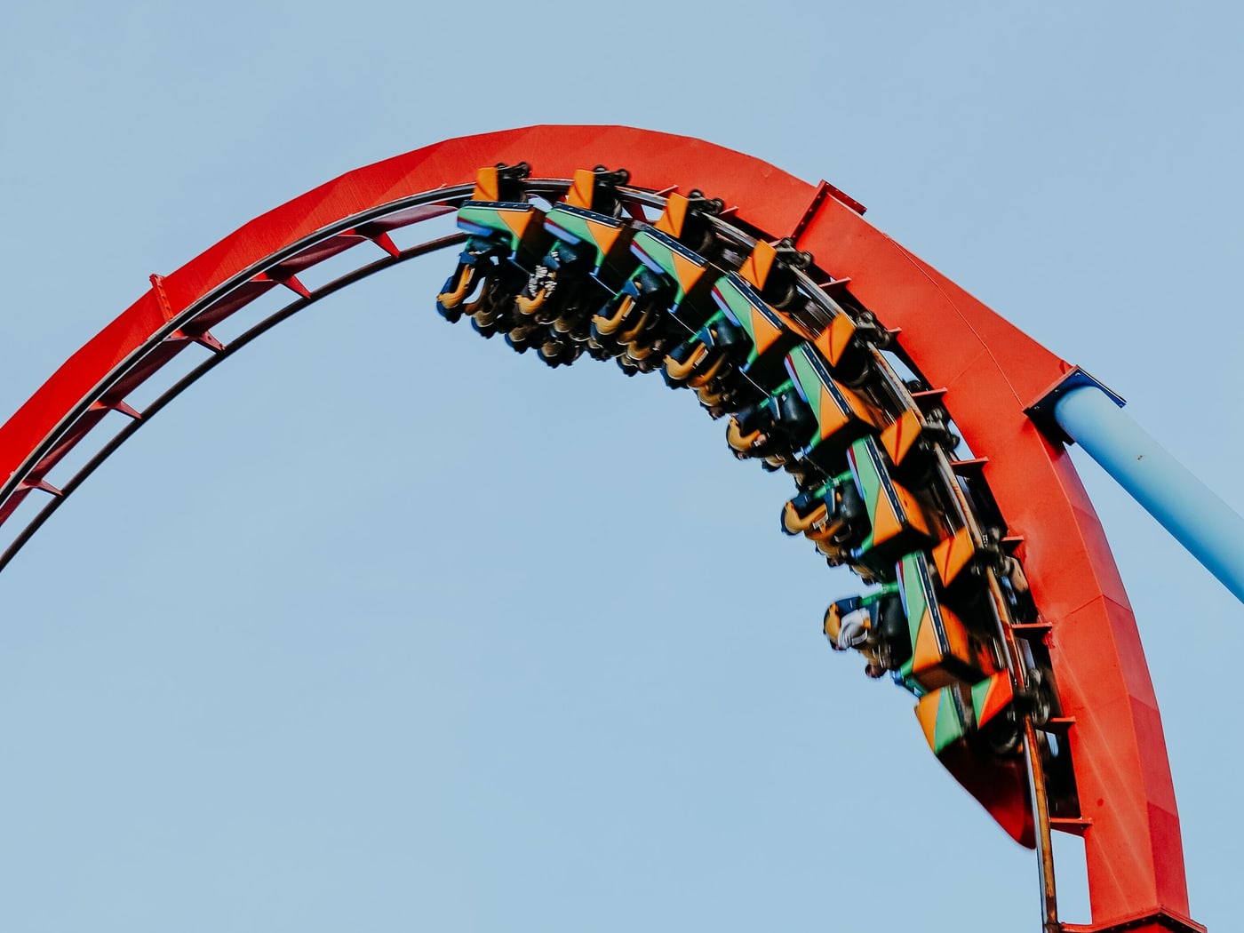 Riders inverted at the top of a red rollercoaster loop against a clear blue sky