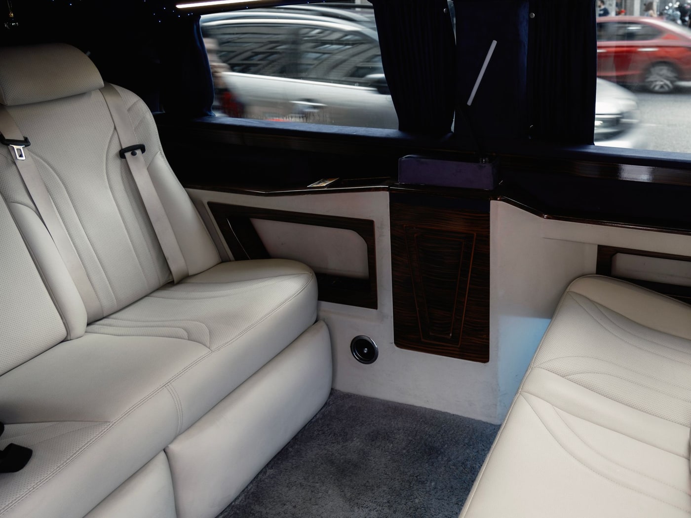 The cream leather rear cabin of a chauffeured van, its side door slid open onto the street