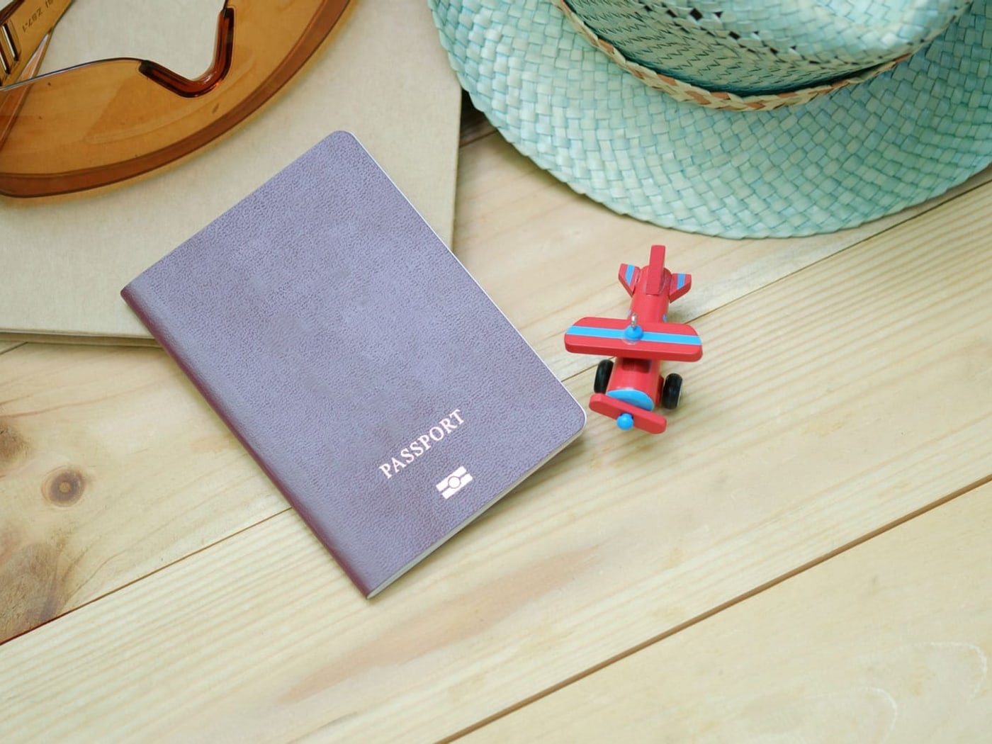 A plain grey passport marked only with the word PASSPORT and the biometric chip symbol, on pale pine beside a kraft notebook